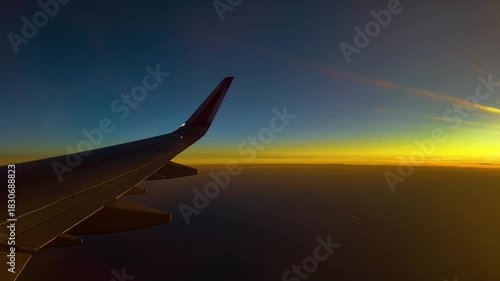 A serene sunrise view from an airplane window, showcasing the aircraft wing, glowing sky, and soft layers of clouds illuminated by warm morning light