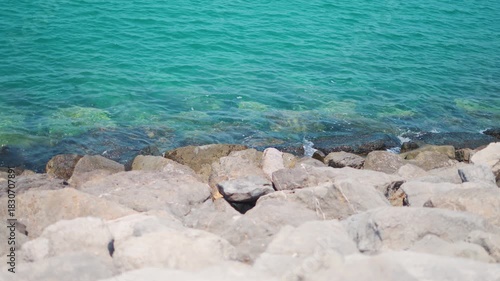 4K Slow motion shot of sea waves hitting rocks on the shore as seen from Abu Dhabi in United Arab Emirates. Scenic view of clear blue sea water hitting the rocks on the side of the sea shore. 