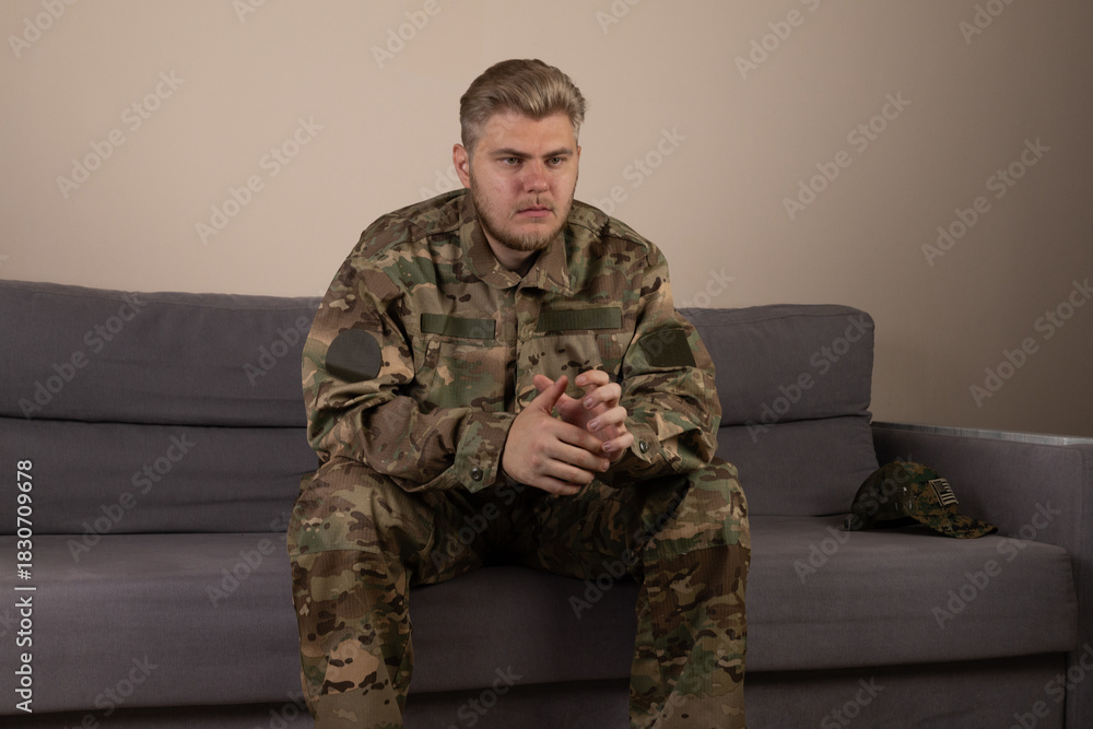 Fototapeta premium A soldier is sitting on a sofa, looking thoughtful