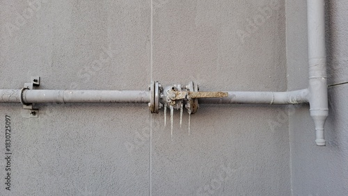 frozen water pipe with icicles on exterior building wall in winter