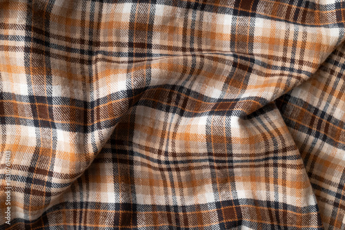Wrinkled in folds plaid brown orange beige flannel cotton fabric, tartan pattern. Close-up of this autumnal natural fabric for shirt, dress, tablecloth, or clothing. Abstract textile background