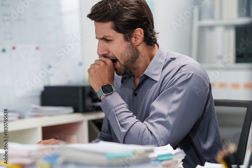 A sleepy businessman lets out a yawn while handling tired paperwork in an overworked, bored office with low energy
