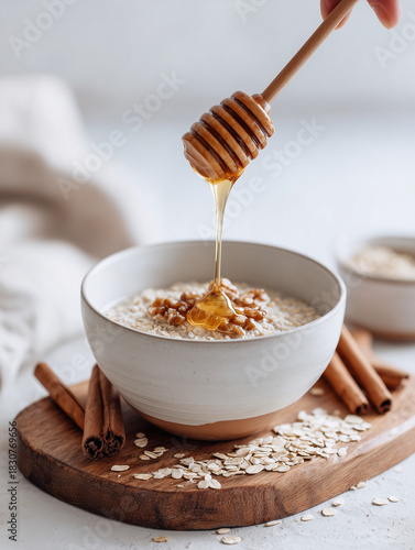 Bowl of oatmeal topped with honey and cinnamon sticks on wooden tray  walnuts