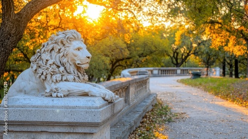 A detailed shot of a lion statue resting on a stone balustrade in a park. The scene is bathed in the warm light of the setting sun.