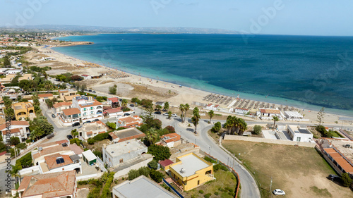 Aerial view of Marzamemi beach, a tourist resort in southern Sicily, in the province of Syracuse, Italy. The coast overlooks the Mediterranean Sea, whose waters are turquoise and crystalline.