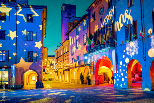 A street and historic buildings of Alba, Italy, illuminated by colorful light projections during a Christmas holidays at twilight.
