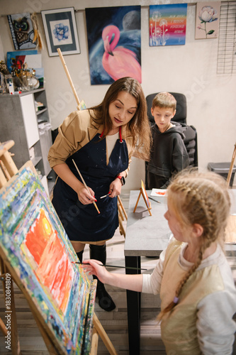 Teacher explains to kids how to draw pictures in art class. School children drawing brush landscapes on easel. Childs enjoy painting in workshop. Art lesson. Education, creativity, learning concept.