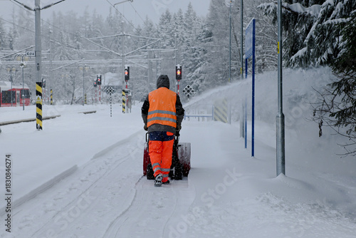 Worker operating a snow blower to clear pathways at a railway station covered in snow