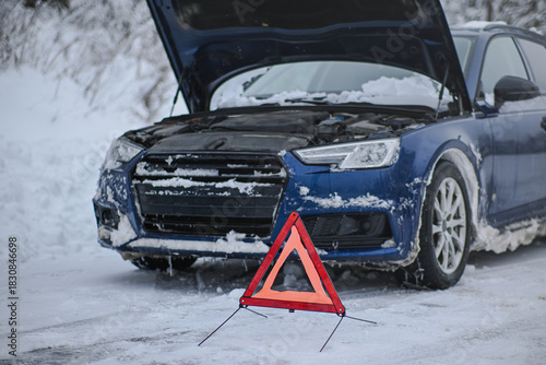 Blue car with open hood and warning triangle on a snowy winter roadside