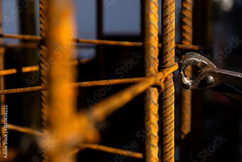 Close-up of a construction worker wearing protective gloves and using pliers to cut or tie steel rebar at a job site. Warm light highlights the texture of rusted metal and manual labor.