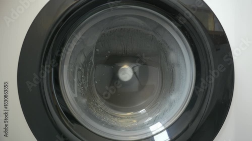 Front-Loading Washing Machine in Action with Clothes Spinning Behind Glass.
Close-up view through the glass door of a modern front-loading washing machine as clothes spin and tumble during a wash.