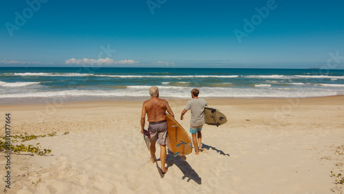 Young and elderly surfers walk with surfing boards on the beach in Brazil