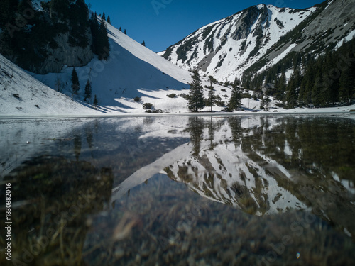 Fotografie Serene winter landscape with a frozen mountain lake reflecting snowy peaks under