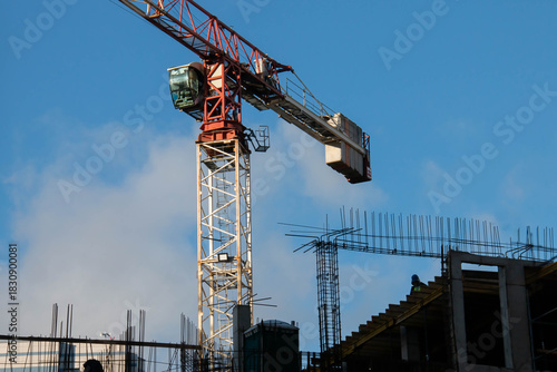 Control Cabin and Counterweight of Red Tower Crane at Construction Site. Monolithic Box with Window Holes and Rebar outlets against Blue Sky background.