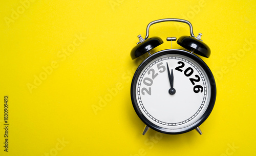 Alarm clock showing 2025 turning into 2026 which symbolizing New Year countdown of time transition, future planning, celebration and year-end change on yellow background and minimal concept.