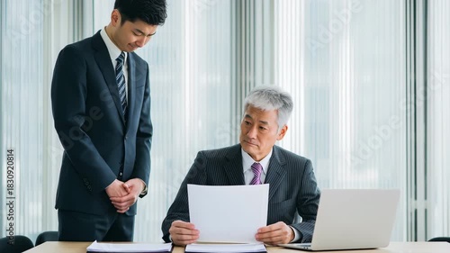 男性が会議室で上司に書類を渡し深く謝罪する場面