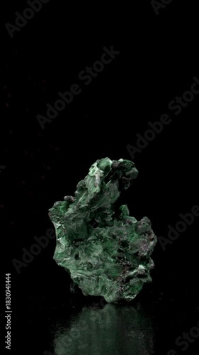Malachite (green copper carbonate hydroxide) Fibrous chatoyant form giving cat's eye effect - rotating slowly against a black background. Vertical.