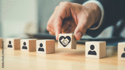 Hand placing wooden block with heart and handshake symbol among people icons