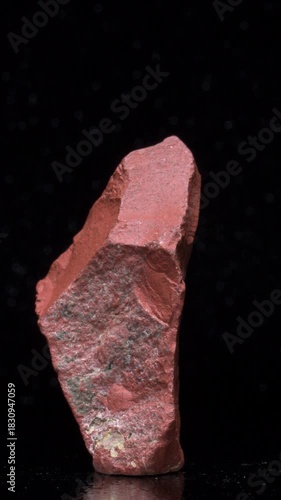 Red Jasper (opaque cryptocrystaline quartz) coloured red by iron inclusions, rotating slowly against a black background. Vertical.