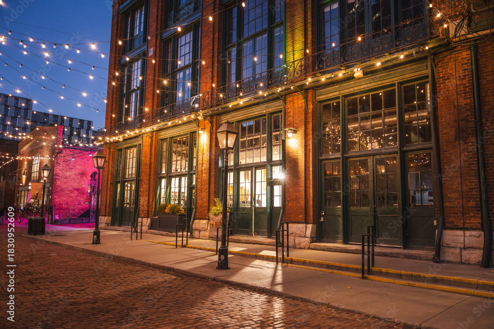 Obraz premium Evening view of historic brick buildings decorated with warm string lights in the Distillery District of Toronto, Canada.