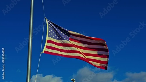 waving American flag on a tall flagpole stretches against a clear blue sky, symbolizing patriotism, freedom, and national pride