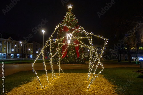 Illuminated holiday light tunnel installation leading toward a decorated Christmas tree with red bows and glowing ornaments in a city square at night.