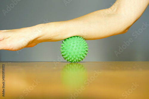 Person performing muscle release exercise by rolling a spiky massage ball under an extended arm. Represents myofascial release therapy, self-massage technique, physical therapy, and wellness self-care