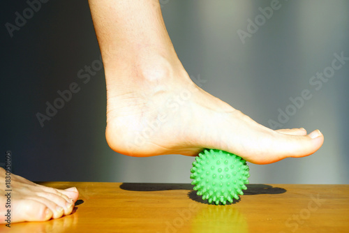 Foot arch rolling over spiky ball for deep tissue foot massage. Illustrates plantar tissue release, reflexology pressure points, self-administered podiatric care, and tension relief technique.