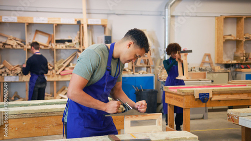 Male Student Studying For Carpentry Apprenticeship At College Using Wood Plane