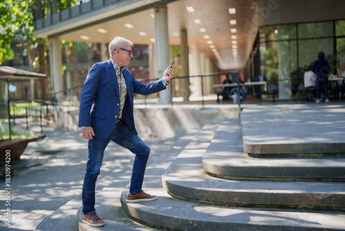 Senior man using smartphone taking selfie on modern steps