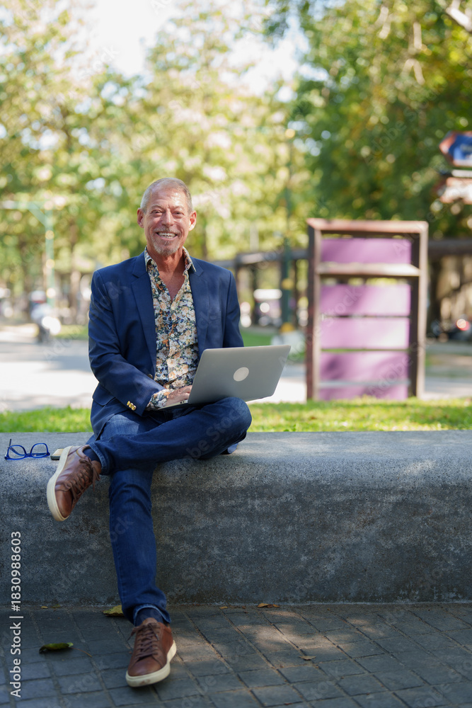 Fototapeta premium Senior man smiling, working outdoors with laptop in park