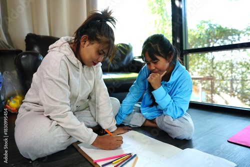 Mother and daughter sitting and drawing/coloring on the living room floor with natural sunlight, demonstrating family love and bonding.