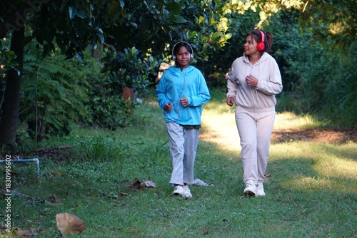 Mother and daughter jogging lightly in the park, both wearing headphones.