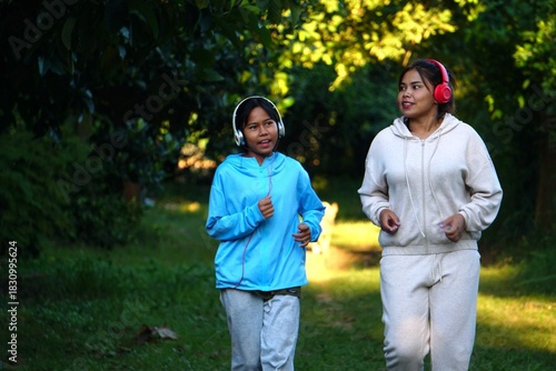 Mother and daughter running together in the park for exercise, with sunlight filtering through the trees.