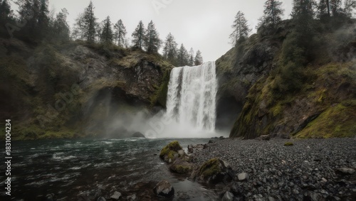 Majestic waterfall cascading down rocky cliffs surrounded by lush green forest under cloudy sky.