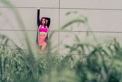 Woman with pink hair posing against urban wall