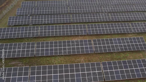 Rows of large solar panels aligned across a grassy field, viewed from above, capturing a renewable energy installation under overcast skies.