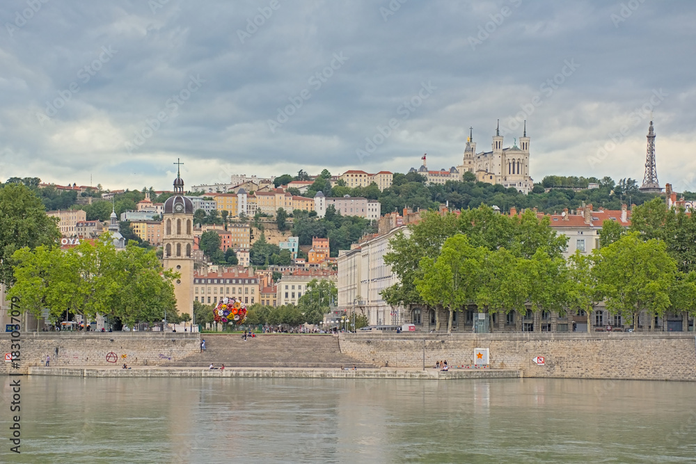 Fototapeta premium Houses and trees along river Rhone, with Basilica of Notre-Dame de Fourvière on a hill in Lyon, France 