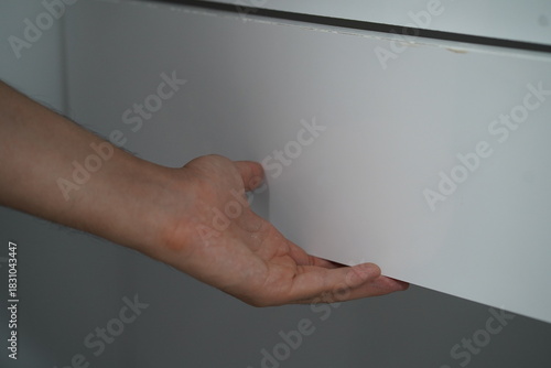 Close Up of a Hand Reaching for a White Drawer with Smooth Surface in a Minimalistic Interior Setting for Stylish Home Organization