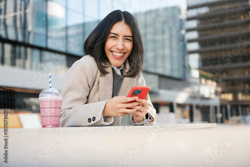 Happy woman using smartphone and enjoying smoothie in city