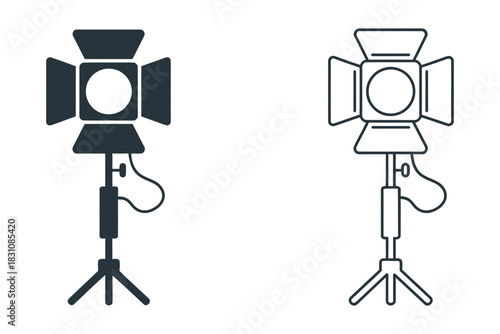 Set of two lighting equipment icons: a solid silhouette of a professional studio spotlight on a tripod and a line art outline, representing film and photography gear.