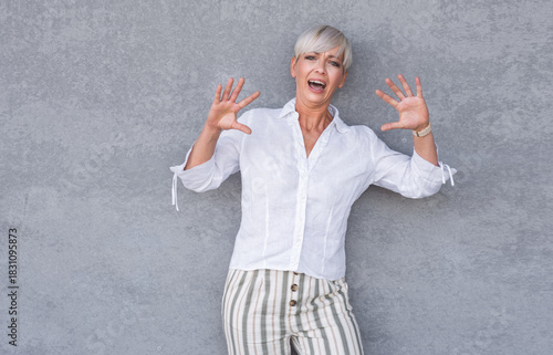 Scared adult woman, being terrible accident, against gray background - wall. Frightened middle age woman