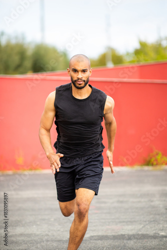 Determined young man sprinting directly at camera on asphalt