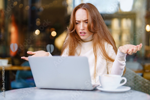 Woman with long hair looking confused while working on a laptop in a cafe during the daytime