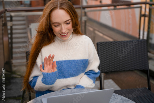 Young woman waving during a video call on a laptop outside in the afternoon