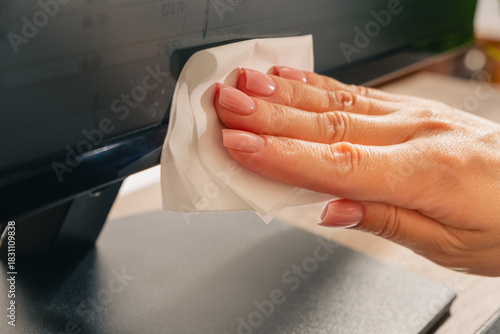 A woman's hand with pink manicured nails wipes the monitor with a paper napkin. Close-up. Photo