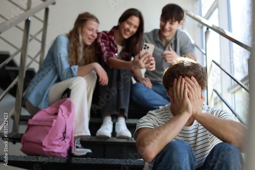 Students bullying their classmate on stairs indoors, selective focus