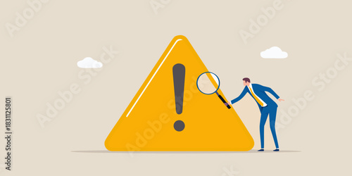 Businessman examines a large yellow warning sign with an exclamation mark using a magnifying glass