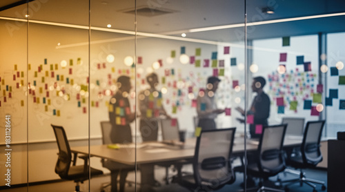 A blurred view of a modern office meeting room with people collaborating around a conference table, surrounded by colorful sticky notes on glass walls.