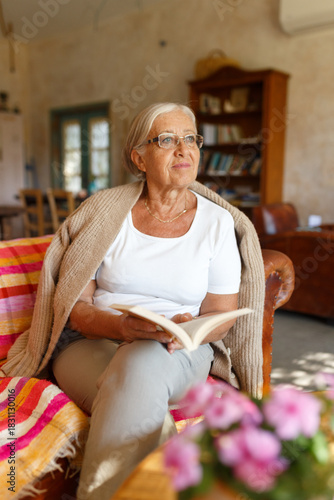 Senior woman relaxing at home reading book daydreaming